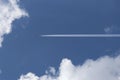 A passenger airplane flying high in the sky among the clouds. Air liner leaving a trace of exhaust gases glowing in the sun. Ecolo Royalty Free Stock Photo