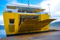 Passenger boat at a port, yellow ferry starts to disembark travellers and cars. Ramp is going down, back of sea and mountains