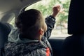 A passenger child in the back seat of a car looks out the car window and wipes the glass with a napkin Royalty Free Stock Photo