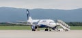 Passenger jet aircraft Airbus A319 of Aurora Airlines on the airfield in cloudy day. Mobile ladder is near by plane.