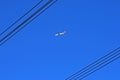 PASSENGER JET IN DEEP BLUE SKY VIEWED BETWEEN OVERHEAD ELECTRICAL CABLES Royalty Free Stock Photo