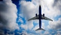 Passenger plane belly view, landing with blue cloudy sky in background.