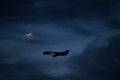 A passenger plane flies against the night sky, lit by the moon Royalty Free Stock Photo