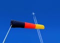 windsock and a passenger plane with vapour trails high in the blue sky Royalty Free Stock Photo