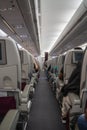 Passenger seat, Interior of airplane with passengers sitting on seats and stewardess walking the aisle in background Royalty Free Stock Photo