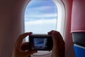 Passenger take a photo graph the beautiful view from porthole of airplane on sky with clouds under sun light Royalty Free Stock Photo