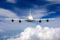 The passenger wide body plane flies high in the blue sky above clouds. Airplane closeup front view