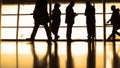 Passengers follow to boarding with baggage in front of window in airport, silhouette, warm