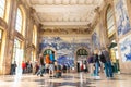 Passengers and tourists looking at large azulejo murals inside the hall of of Saint Benedict Railway Station in Porto