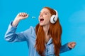 Passionate and carefree cute foxy european redhead woman in pyjama, close eyes wearing headphones, listening music