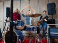 Passionate emotional female drummer with her bandmates practicing in rehearsal room Royalty Free Stock Photo