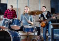 Passionate emotional female drummer with her bandmates practicing in rehearsal room Royalty Free Stock Photo