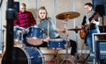 Passionate emotional female drummer with her bandmates practicing in rehearsal room Royalty Free Stock Photo