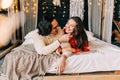 Passionate romantic couple spending home with garlands. Young woman and man are lying on bed in sweaters and hugging