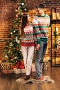 Passionate romantic couple is spending time together before New Year near beautiful Christmas tree at home. Young woman