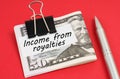 On a red background lies a pen and dollars clamped with a clip with the inscription on paper - Income from royalties Royalty Free Stock Photo