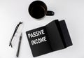 PASSIVE INCOME written text in small black notebook with coffee , pen and glasess on white background. Black-white style Royalty Free Stock Photo