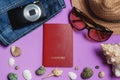 Passport, Jeans, Sunglasses, Photo Camera, Brown Hat, Seashells on Lilac Background. Top View Travel Concept.