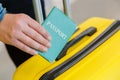 Passport in male hand behind suitcases before airplane trip in airport. Man holding green passport with ticket on yellow Royalty Free Stock Photo