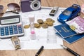 Passport, money, camera, watch, calculator, glasses, calendar toy car on wooden table.