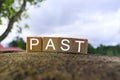 Past text on wooden cube block on top of stone with blurred sky background