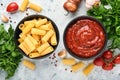 Pasta background. Pasta rigatoni, tomato ketchup sauce, olive oil, spices, parsley, and fresh tomatoes on light grey old slate,