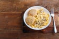 Pasta in a creamy sauce with mushrooms and chicken meatballs in a beige plate on a wooden table next to a fork. copy space Royalty Free Stock Photo