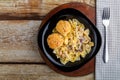 Pasta in a creamy sauce with mushrooms and chicken meatballs in a black plate on a wooden table on a napkin near the Royalty Free Stock Photo