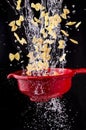 Pasta falls into the red colander with splashes of water Royalty Free Stock Photo