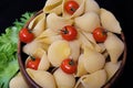 Pasta in the form of shells in a round wooden bowl with cherry tomatoes on a black background. Culinary background Royalty Free Stock Photo