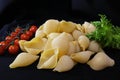 Pasta in the form of shells in a round wooden bowl with cherry tomatoes on a black background. Culinary background Royalty Free Stock Photo