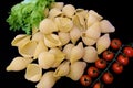 Pasta in the form of shells in a round wooden bowl with cherry tomatoes on a black background. Culinary background Royalty Free Stock Photo