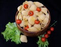 Pasta in the form of shells in a round wooden bowl with cherry tomatoes on a black background. Culinary background Royalty Free Stock Photo