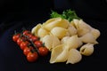 Pasta in the form of shells in a round wooden bowl with cherry tomatoes on a black background. Culinary background Royalty Free Stock Photo