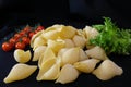 Pasta in the form of shells in a round wooden bowl with cherry tomatoes on a black background. Culinary background Royalty Free Stock Photo