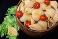 Pasta in the form of shells in a round wooden bowl with cherry tomatoes on a black background. Culinary background Royalty Free Stock Photo