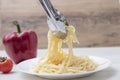 Pasta with gralic and chili. Hand with tongs move spaghetti with butter to a white plate on wood background