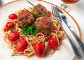 Pasta with meatballs and tomato sauce. Decorated with greens and roasted cherry tomatoes. In the original plate with cutlery. Royalty Free Stock Photo