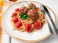 Pasta with meatballs and tomato sauce. Decorated with greens and roasted cherry tomatoes. In the original plate with cutlery. View Royalty Free Stock Photo