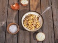 Pasta with minced turkey in a deep ceramic bowl and a tablespoon, an onion cut in halves on a wooden plank table