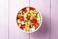 Pasta salad with quail eggs, mozzarella, cherry tomatoes and capers in bowl on purple wooden background Royalty Free Stock Photo