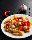 Pasta salad with tomato, pepper and mozzarella balls in plate on dark wooden background Royalty Free Stock Photo