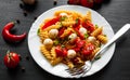 Pasta salad with tomato, pepper and mozzarella balls in plate on dark wooden background Royalty Free Stock Photo