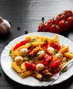 Pasta salad with tomato, pepper and mozzarella balls in plate on dark wooden background Royalty Free Stock Photo