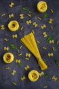 Pasta in the shape of a butterfly, spiral, nests and spaghetti, red and black peppercorns, salt on a dark background