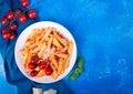 Pasta penne with tomato sauce, fresh basil, roasted tomatoes and parmesan on the blue background