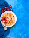 Pasta penne with tomato sauce, fresh basil, roasted tomatoes and parmesan on the blue background