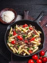 Pasta with tomatoes and meat on dark rustic background.