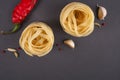 Pasta Top view. Two Fettuccine nest on a gray background with spices. Hot peppers, fennel seeds and chilli peppers. Flat lay