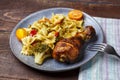 Pasta with vegetables and cherry tomatoes with baked chicken leg on the table next to a light napkin and fork. Royalty Free Stock Photo